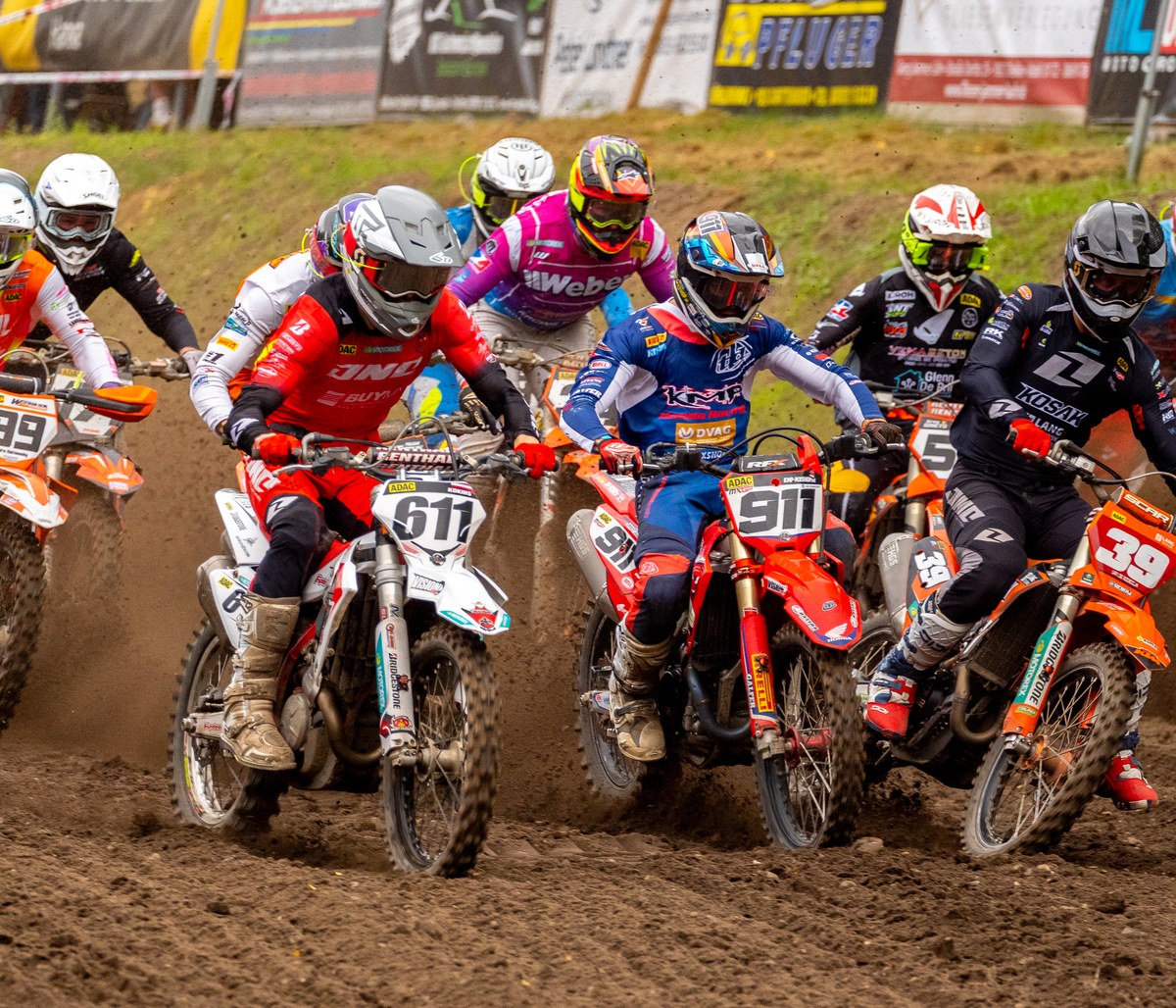 Startfeld beim Motocross: neun Fahrer nebeneinander in der ersten Kurve